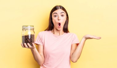 Genç İspanyol kadın şaşırmış ve şok olmuş görünüyor. Çenesi düşmüş ve elinde bir nesne tutuyor. kahve çekirdeği konsepti