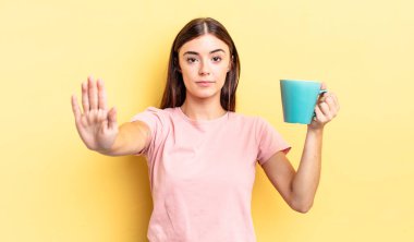 Genç İspanyol kadın ciddi görünüyor. Avuç içini gösteriyor. Durdurma hareketi yapıyor. Kahve fincanı konsepti