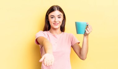 Genç İspanyol kadın mutlu bir şekilde gülümsüyor ve bir konsept sunuyor. Kahve fincanı konsepti