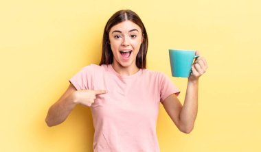 Genç İspanyol kadın kendini mutlu hissediyor ve heyecanla kendini işaret ediyor. Kahve fincanı konsepti