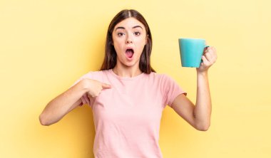 Genç İspanyol kadın şok olmuş ve ağzı açık, kendini işaret ederek şaşırmış görünüyor. Kahve fincanı konsepti