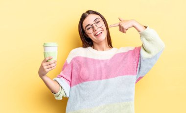 Genç İspanyol kadın kendine güvenerek gülümsüyor ve kendi gülüşünü gösteriyor. kahve konseptini kaldır.