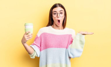 Genç İspanyol kadın şaşırmış ve şok olmuş görünüyor. Çenesi düşmüş ve elinde bir nesne tutuyor. kahve konseptini kaldır.
