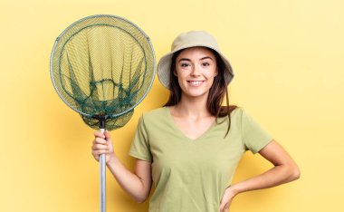 Genç İspanyol kadın mutlu bir şekilde gülümsüyor, eli kalçasında ve kendine güvenen balık ağı konseptiyle.