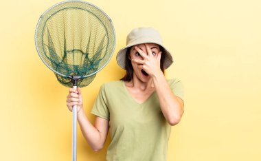 Genç İspanyol kadın şok olmuş, korkmuş ya da korkmuş görünüyor, yüzünü balık ağı konseptiyle kapatıyor.