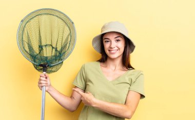 Genç İspanyol kadın neşeyle gülümsüyor, mutlu hissediyor ve balık ağı kavramını işaret ediyor.