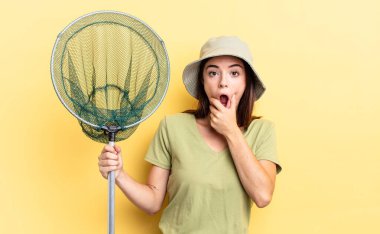 Ağzı ve gözleri sonuna kadar açık ve eli çenesinde balık ağı kavramı olan genç İspanyol kadın.