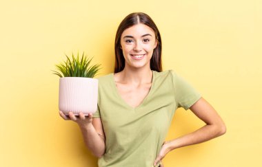 Genç İspanyol kadın mutlu bir şekilde gülümsüyor, eli kalçasında ve kendinden emin. bitki otu konsepti