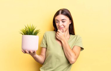 Genç İspanyol kadın mutlu ve kendinden emin bir ifadeyle gülümsüyor. Elleri çenesinde. bitki otu konsepti