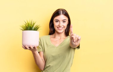 Genç İspanyol kadın gülümsüyor ve arkadaş canlısı görünüyor, bir numarayı gösteriyor. bitki otu konsepti