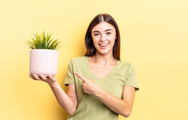 Genç İspanyol kadın neşeyle gülümsüyor, mutlu hissediyor ve bir tarafı işaret ediyor. bitki otu konsepti