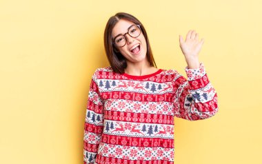 Genç İspanyol kadın mutlu bir şekilde gülümsüyor, el sallıyor, sizi selamlıyor ve selamlıyor. Chistmas ve yeni yıl konsepti