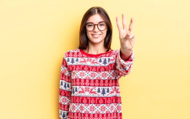 Genç İspanyol kadın gülümsüyor ve arkadaş canlısı görünüyor, üç numarayı gösteriyor. Chistmas ve yeni yıl konsepti