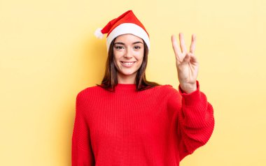 Genç İspanyol kadın gülümsüyor ve arkadaş canlısı görünüyor, üç numarayı gösteriyor. Chistmas ve yeni yıl konsepti