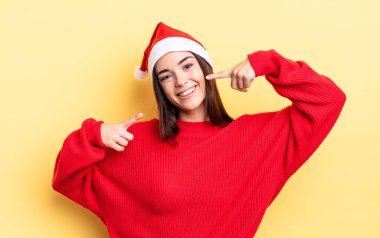 Genç İspanyol kadın kendine güvenerek gülümsüyor ve kendi gülüşünü gösteriyor. Chistmas ve yeni yıl konsepti