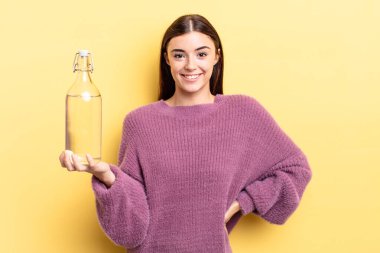 Genç İspanyol kadın mutlu bir şekilde gülümsüyor, eli kalçasında ve kendinden emin. su şişesi kavramı