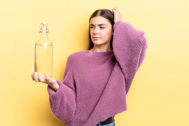 Genç İspanyol kadın şaşkın ve kafası karışık, kaşınan bir kafa hissediyor. su şişesi kavramı