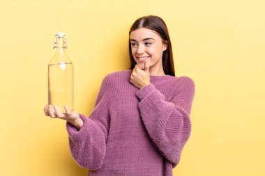 Genç İspanyol kadın mutlu ve kendinden emin bir ifadeyle gülümsüyor. Elleri çenesinde. su şişesi kavramı