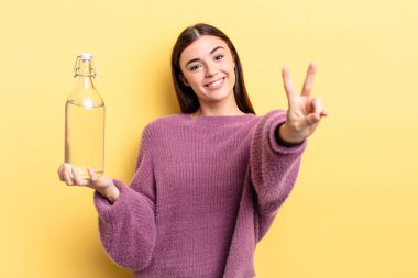 Genç İspanyol kadın gülümsüyor ve mutlu görünüyor, zafer ya da barış işareti yapıyor. su şişesi kavramı