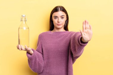 Genç İspanyol kadın ciddi görünüyor. Avuç içini gösteriyor. Durdurma hareketi yapıyor. su şişesi kavramı
