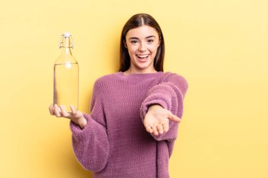 Genç İspanyol kadın mutlu bir şekilde gülümsüyor ve bir konsept sunuyor. su şişesi kavramı