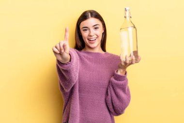 Genç İspanyol kadın gülümsüyor ve arkadaş canlısı görünüyor, bir numarayı gösteriyor. su şişesi kavramı