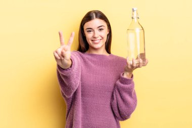 Genç İspanyol kadın gülümsüyor ve arkadaş canlısı görünüyor, iki numarayı gösteriyor. su şişesi kavramı