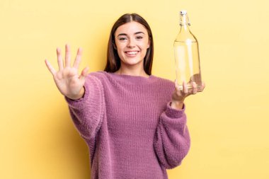 Genç İspanyol kadın gülümsüyor ve arkadaş canlısı görünüyor, beş numarayı gösteriyor. su şişesi kavramı