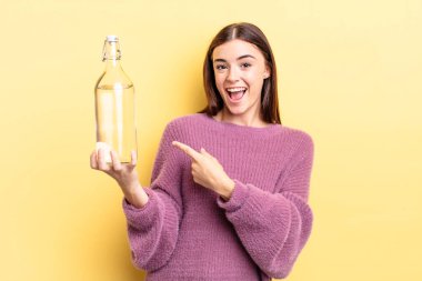 Genç İspanyol kadın heyecanlı ve şaşırmış görünüyor. su şişesi kavramı