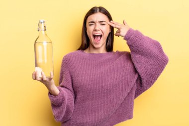 Genç İspanyol kadın mutsuz ve stresli görünüyor, intihar jesti silah işareti yapıyor. su şişesi kavramı