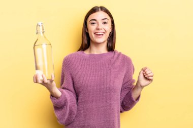 Genç İspanyol kadın mutlu ve hoş bir şekilde şaşırmış görünüyor. su şişesi kavramı