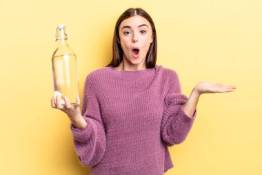 Genç İspanyol kadın şaşırmış ve şok olmuş görünüyor. Çenesi düşmüş ve elinde bir nesne tutuyor. su şişesi kavramı