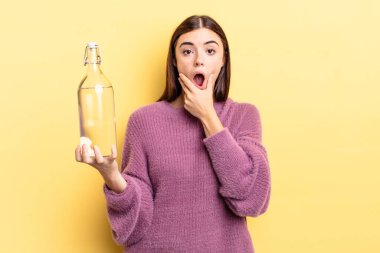 Ağzı ve gözleri sonuna kadar açık ve eli çenesinde olan genç İspanyol kadın. su şişesi kavramı