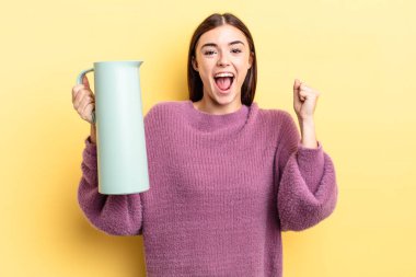 Genç İspanyol kadın şokta, gülüyor ve başarıyı kutluyor. Kahve termosu kavramı