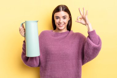 Genç İspanyol kadın kendini mutlu hissediyor, iyi bir jestle onaylıyor. Kahve termosu kavramı