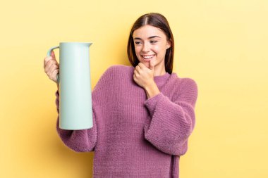 Genç İspanyol kadın mutlu ve kendinden emin bir ifadeyle gülümsüyor. Elleri çenesinde. Kahve termosu kavramı