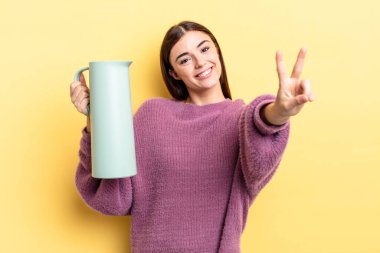 Genç İspanyol kadın gülümsüyor ve mutlu görünüyor, zafer ya da barış işareti yapıyor. Kahve termosu kavramı