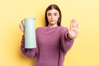 Genç İspanyol kadın ciddi görünüyor. Avuç içini gösteriyor. Durdurma hareketi yapıyor. Kahve termosu kavramı