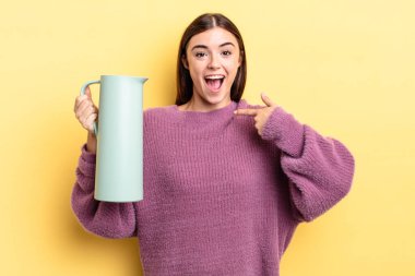 Genç İspanyol kadın kendini mutlu hissediyor ve heyecanla kendini işaret ediyor. Kahve termosu kavramı