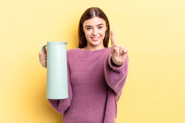 Genç İspanyol kadın gülümsüyor ve arkadaş canlısı görünüyor, bir numarayı gösteriyor. Kahve termosu kavramı