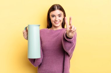 Genç İspanyol kadın gülümsüyor ve arkadaş canlısı görünüyor, iki numarayı gösteriyor. Kahve termosu kavramı