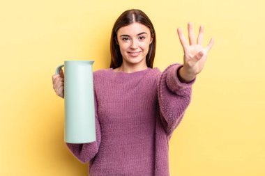 Genç İspanyol kadın gülümsüyor ve arkadaş canlısı görünüyor, dört numarayı gösteriyor. Kahve termosu kavramı