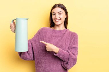 Genç İspanyol kadın neşeyle gülümsüyor, mutlu hissediyor ve bir tarafı işaret ediyor. Kahve termosu kavramı