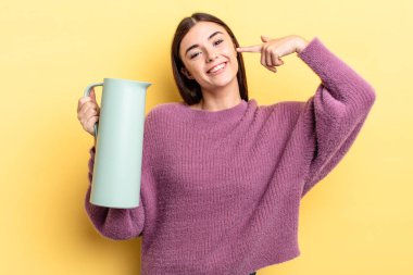 Genç İspanyol kadın kendine güvenerek gülümsüyor ve kendi gülüşünü gösteriyor. Kahve termosu kavramı