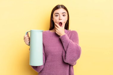 Ağzı ve gözleri sonuna kadar açık ve eli çenesinde olan genç İspanyol kadın. Kahve termosu kavramı