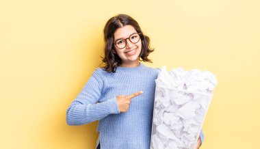 Genç İspanyol kadın neşeyle gülümsüyor, mutlu hissediyor ve başarısız çöp konseptine işaret ediyor.