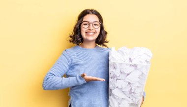 Genç İspanyol kadın neşeyle gülümsüyor, mutlu hissediyor ve bir konsepti başarısız çöp konsepti gösteriyor.