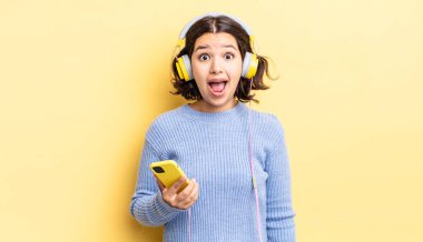 Genç İspanyol kadın çok şaşırmış ya da şok olmuş görünüyor. kulaklıklar ve akıllı telefon konsepti