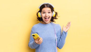 Genç İspanyol kadın kendini mutlu hissediyor ve inanılmaz bir şeye hayret ediyor. kulaklıklar ve akıllı telefon konsepti