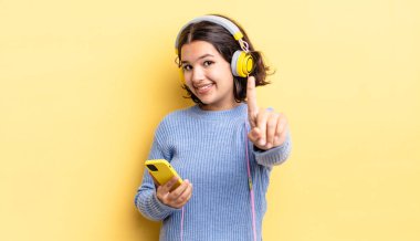 Genç İspanyol kadın gururla gülümsüyor ve kendinden emin bir numara oluyor. kulaklıklar ve akıllı telefon konsepti